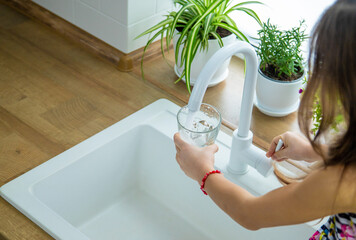 Children picks up a glass of water from the tap. Selective focus.