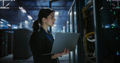 Naklejka na ściany i meble Technician uses a laptop computer to check and monitor server racks in a large data center, hardware installation, network devices diagnosttics, system check. Server room with mainframes.