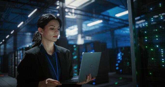 Technician uses a laptop computer to check and monitor server racks in a large data center, hardware installation, network devices diagnosttics, system check. Server room with mainframes.