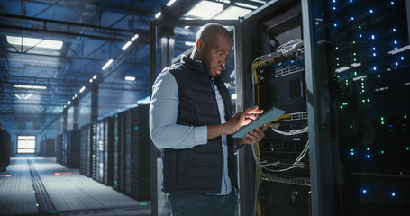 Data center technician inspects server racks, checks network cables, and uses a tablet to monitor hardware status. Rows of illuminated servers, digital infrastructure, and secure network operations.