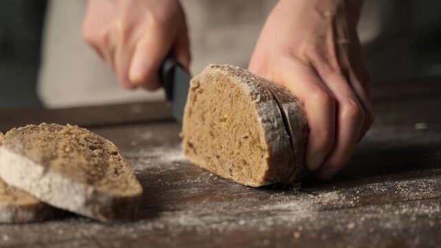 Professional baker slicing fresh homemade rye bread with a knife on a wooden cutting board in a rustic bakery kitchen