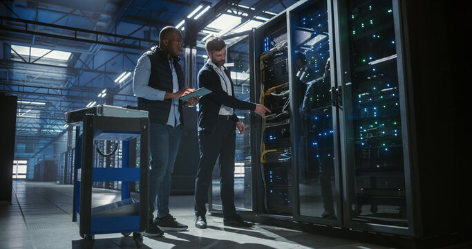 Technicians inspect and maintain server racks in a modern data center, using a tablet to monitor equipment, check connections,  operation of network hardware, mainframe, server racks.