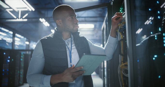 Data center technician inspects server racks, checks network cables, and uses a tablet to monitor hardware status. Rows of illuminated servers, digital infrastructure, and secure network operations.