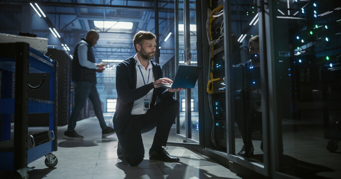 Technician uses a laptop of server rack systems in a data center, analysis of device connections, network cables, electronics for secure business infrastructure, it service, and software operation.