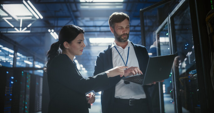 Two specialists use a laptop to review server rack electronics, check device connections, and monitor network cables in data center, business infrastructure, it service, saas software operation