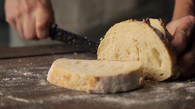 Baker slicing fresh homemade crusty bread with a knife on a rustic wooden cutting board for a healthy breakfast