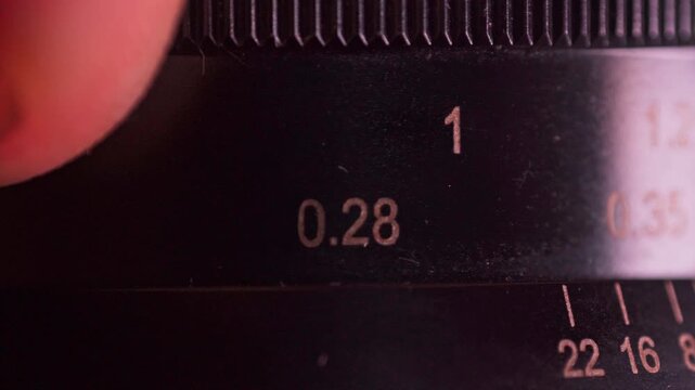 Extreme macro footage of a hand rotating the aperture ring on a classic manual camera lens with visible scale markings.