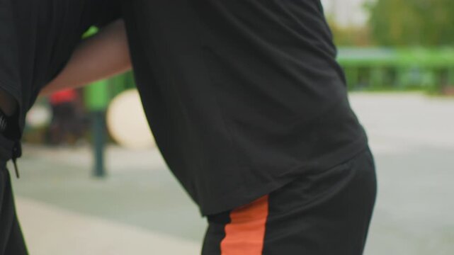 close quarter arm control white man training wrist turn elbow escape partner guided technique tattoo sleeve detail orange shorts contrast green park background steady pace safety emphasis