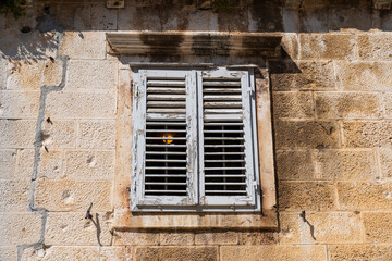 Fototapeta premium Weathered white wooden shutters on an old stone wall, rustic Mediterranean architectural detail in bright sunlight.