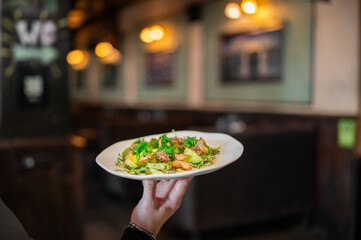Hand holding a plate with a fresh shrimp and avocado salad in a restaurant setting. Shallow depth of field with a blurred interior background © pavel siamionov