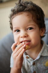Toddler boy with curly hair eating cookie, close-up portrait looking at camera