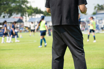 Fototapeta premium Asian parents watching and supporting their children playing football on a sunny afternoon at a local community tournament.