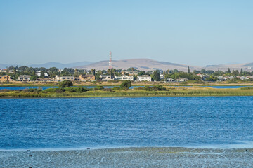 Naklejka premium South Africa,Cape Town,A serene lakeside view with a distant town and mountains under a clear blue sky