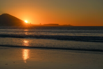 Obraz premium South Africa,Cape Town,Sunset over a calm ocean with waves gently rolling onto the beach, reflecting golden light.