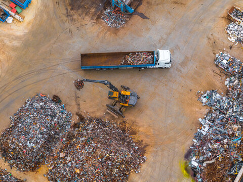 Aerial view of a sprawling scrapyard where a yellow crane loads metal into a truck against a backdrop of scattered debris, Avezzano, Abruzzo, Italy.