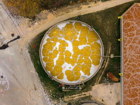 Aerial view of the circular water treatment plant tank with foaming water, a stark contrast against the surrounding industrial landscape, Avezzano, Abruzzo, Italy.