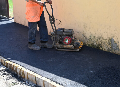  Worker uses a compactor to prepare asphalt surface on a path by a wall in a construction area