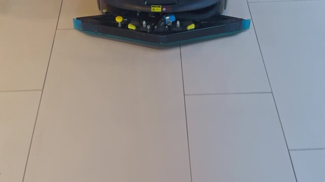 Robotic cleaning device. Automated floor cleaning machine smoothly operating on ceramic tiles in retail corridor at evening hours