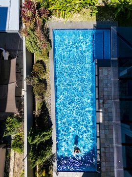 Aerial view of a person swimming in a pristine blue pool, bordered by verdant plants and sleek architecture, Kuala Lumpur, Federal Territory of Kuala Lumpur, Malaysia.