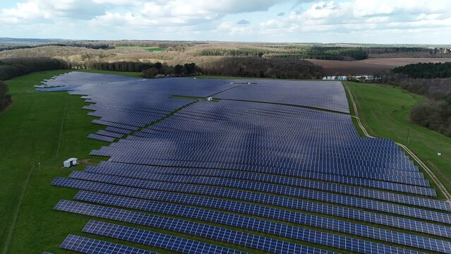 Aerial view of rows of solar panels gleam under the diffused sunlight, contrasting with the surrounding verdant fields and distant woodlands, Mansfield, England, United Kingdom.