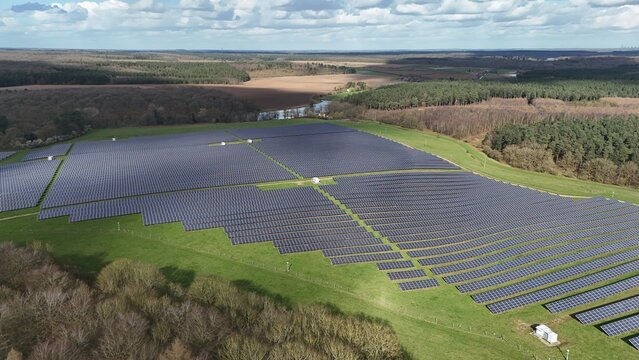 Aerial view of the vast solar farm, panels shimmering darkly against the green hillside, edged by woods, Mansfield, England, United Kingdom.