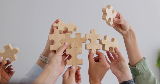 Hands of business people lift and connect wooden puzzle pieces toward team solution. Raised hands join jigsaw parts to collaborate in teamwork, plan project strategy and build partnership together