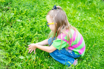 Fototapeta premium child exploring natural world with curiosity and focus, Young girl carefully examining small plants and flowers in lush green field, Outdoor moment wonder, sitting on grass, environmental awareness