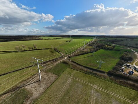 Aerial view of modern pylons stride across the verdant fields, cutting a path through the heart of the countryside, Eakring, United Kingdom.