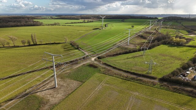 Aerial view of gleaming, modern T-pylons stride across verdant fields near Kirklington Road, a symbol of energy and progress, Eakring, United Kingdom.
