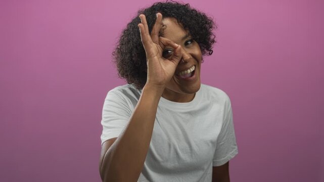 Young woman with curly hair in white tshirt makes ok sign with hand in studio setting; approval optimism.