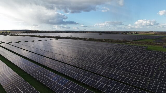 Aerial view of rows of solar panels reflecting the sky, contrasting with the green grass and distant tree line, Goldbeck Solar Crifton South solar farm, Newark, United Kingdom.