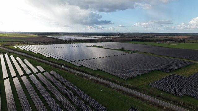 Aerial view of vast solar arrays gleam under a patchy sky, juxtaposed against verdant fields and distant structures, Newark, United Kingdom.