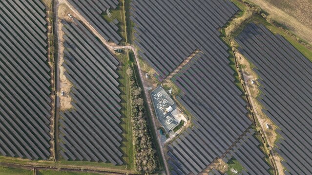 Aerial view of rows of solar panels reflecting the sky, interspersed with verdant patches of grass and small buildings, Halloughton, Southwell, United Kingdom.