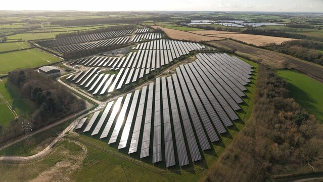 Aerial view of rows of solar panels glinting under the sunlight amidst the patchwork of green fields and golden stubble, Halloughton, Southwell, United Kingdom.