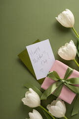 Fototapeta premium Happy Mother's Day note and wrapped gift styled with white tulips, satin ribbon and green envelope for a soft, vertical elegant spring celebration