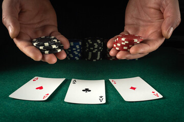 Obraz premium Two hands are seen holding stacks of red, black, and white poker chips. Three playing cards lay face up on the green table. The scene shows the action of a card game in low light
