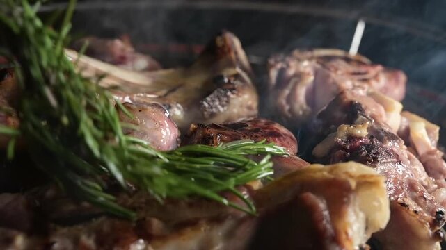 Close-up video of Easter lamb cooking on a barbecue grill while being brushed with fresh rosemary. Juicy meat sizzling over heat with aromatic herbs. Concept of traditional holiday cooking