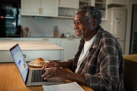 Smiling senior man working on laptop in home kitchen