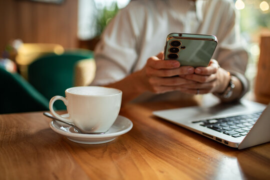 Young professional using smartphone with laptop in coffee shop
