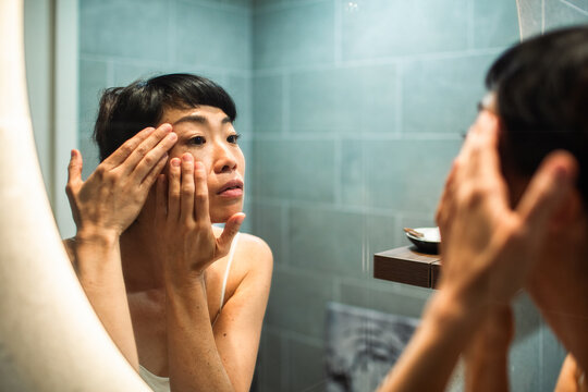 Woman applying eye cream in bathroom mirror