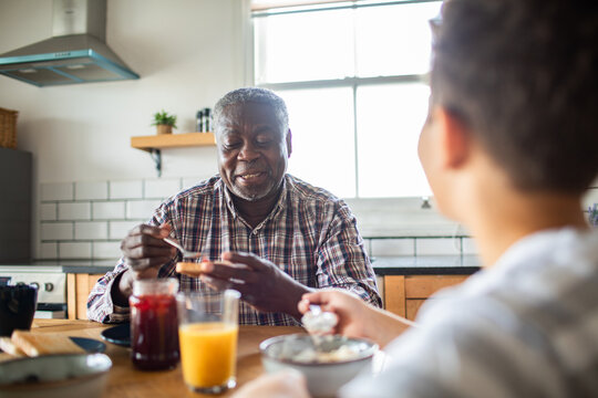 Grandfather spreading jam on toast at breakfast with grandson in home kitchen