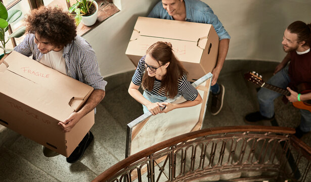 Group of friends carrying moving boxes up apartment stairwell