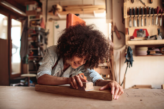 Smiling woodworker sanding plank in home workshop