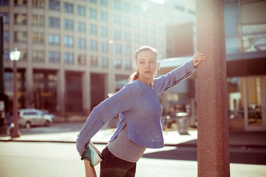 Female runner stretching with headphones on urban street