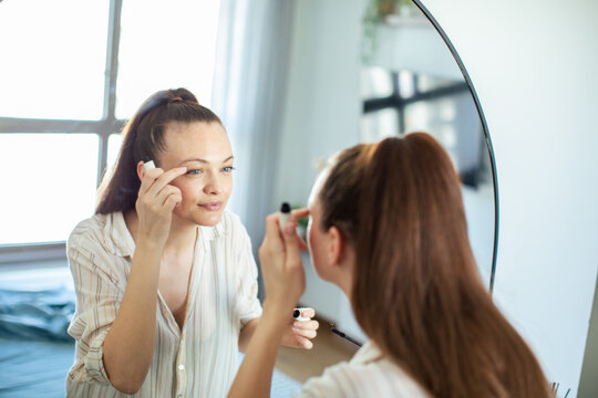 Young woman applying mascara in bedroom mirror