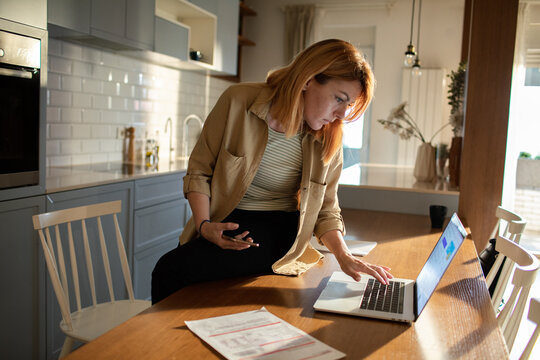 Woman paying household bills on laptop in modern kitchen