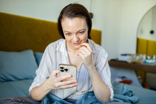 Young woman texting on smartphone in bed at home