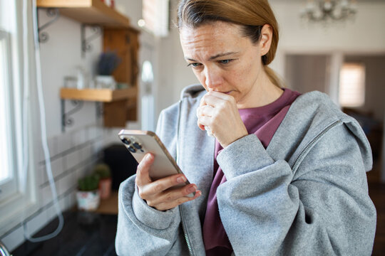 Concerned woman reading message on smartphone in home kitchen