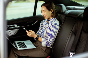 Korean woman uses laptop and phone while sitting in a car during a busy day