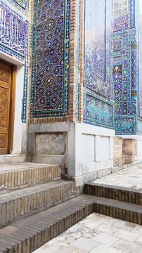 Three majestic mausoleums facing each other in Shah-i-Zinda necropolis. Golden morning sunlight accentuates rich turquoise mosaics, intricate geometric tile patterns, arches. Samarkand, Uzbekistan.